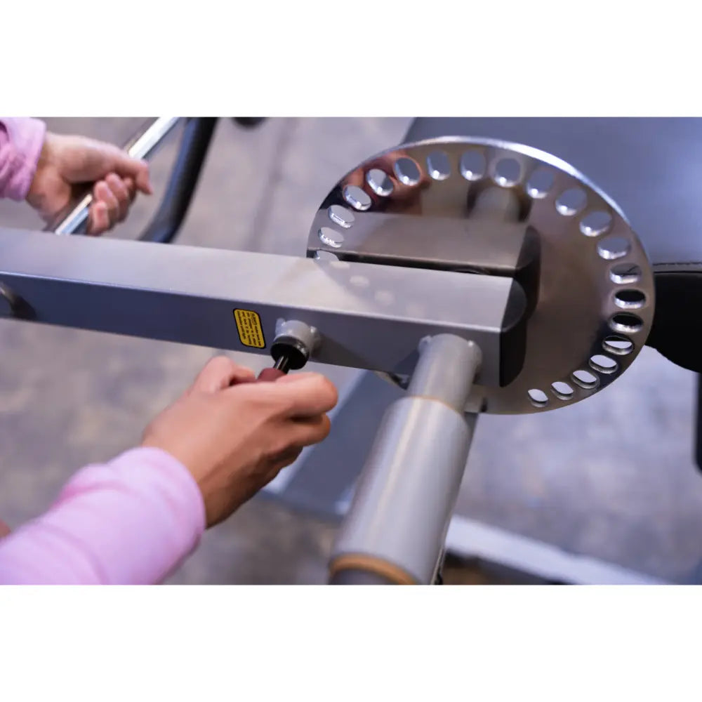 Adjusting resistance on a silver gym machine with a circular plate and handle.