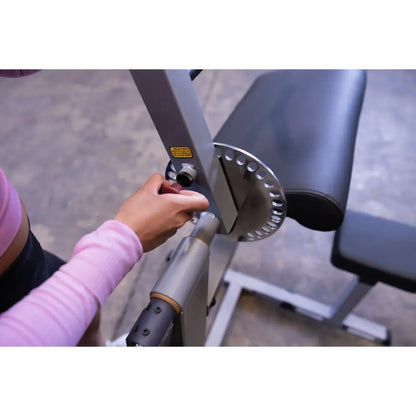 Adjusting a gym bench angle with a silver knob, wearing a pink sleeve.