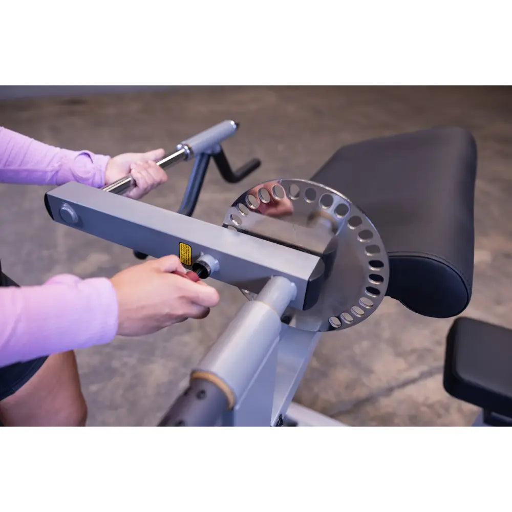 Adjusting arm curl machine with silver adjustment plate in a gym setting.
