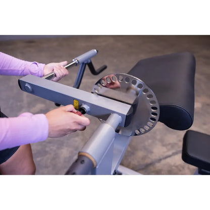 Adjusting arm curl machine with silver adjustment plate in a gym setting.