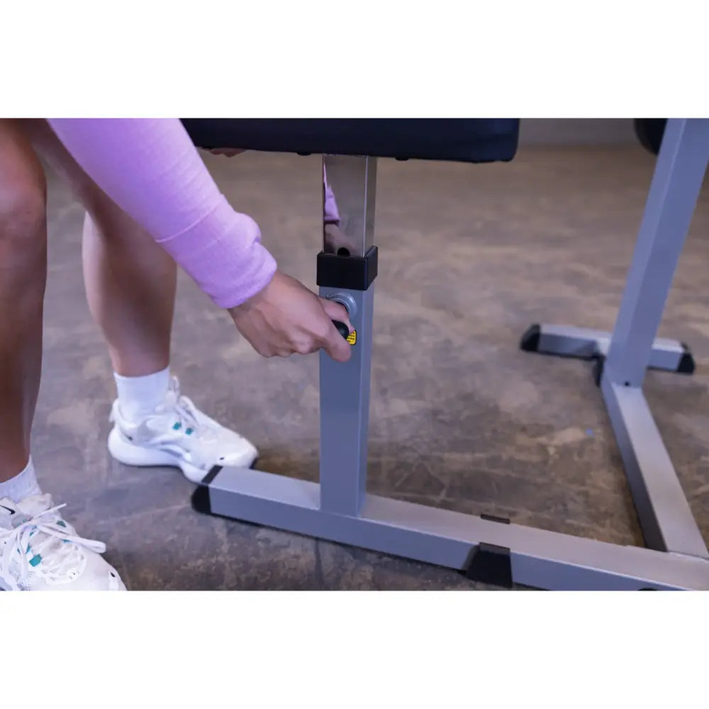 Adjustable weight bench being set to desired height by person in white sneakers and purple sleeve.