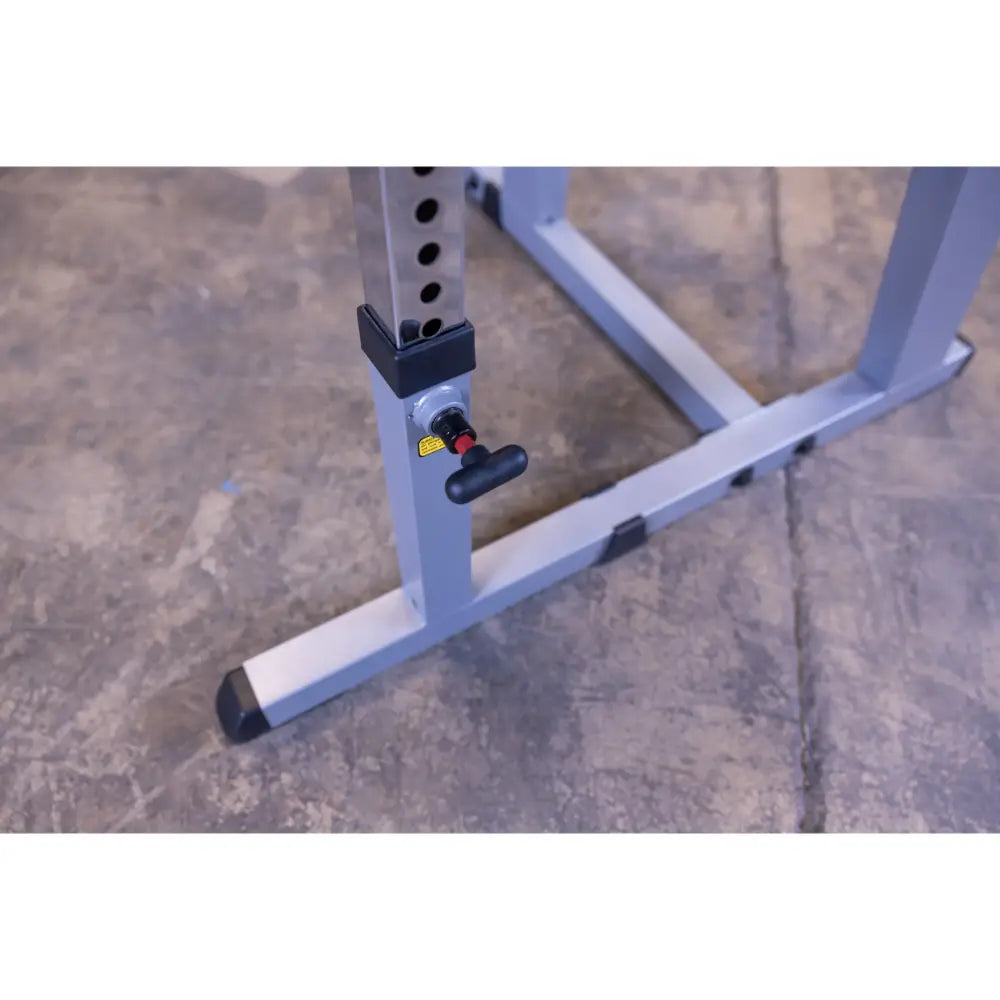 Adjustable squat rack base with safety pin on concrete floor.