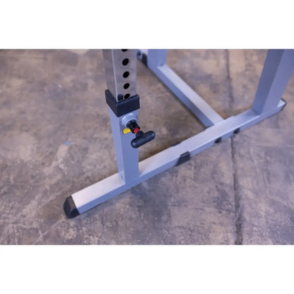 Adjustable squat rack base with safety pin on concrete floor.