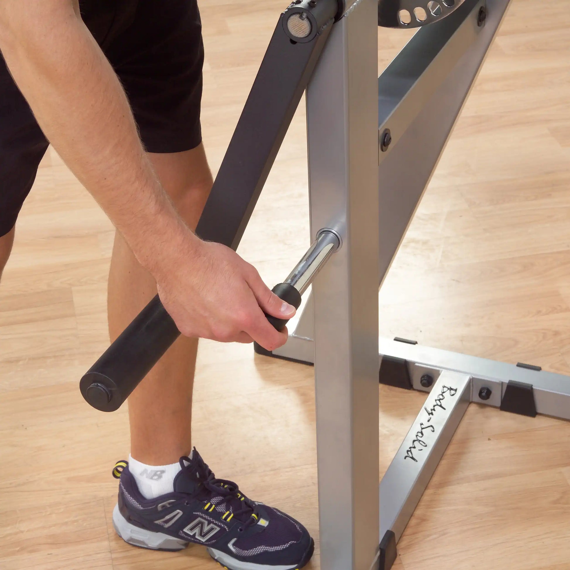 Man adjusting Body-Solid weight bench with black handle on wooden floor.