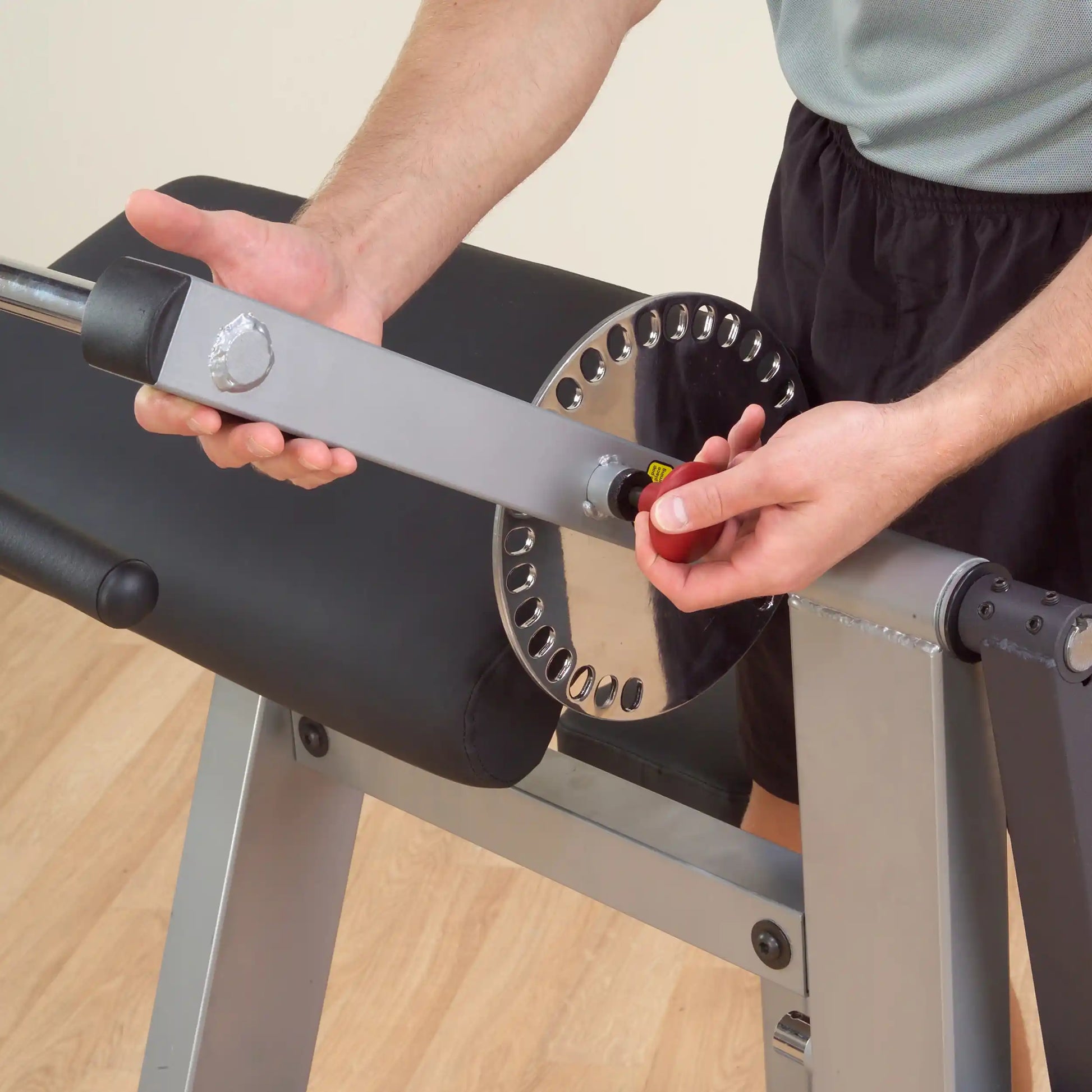 Adjustable weight bench with chrome adjustment dial being set by person.