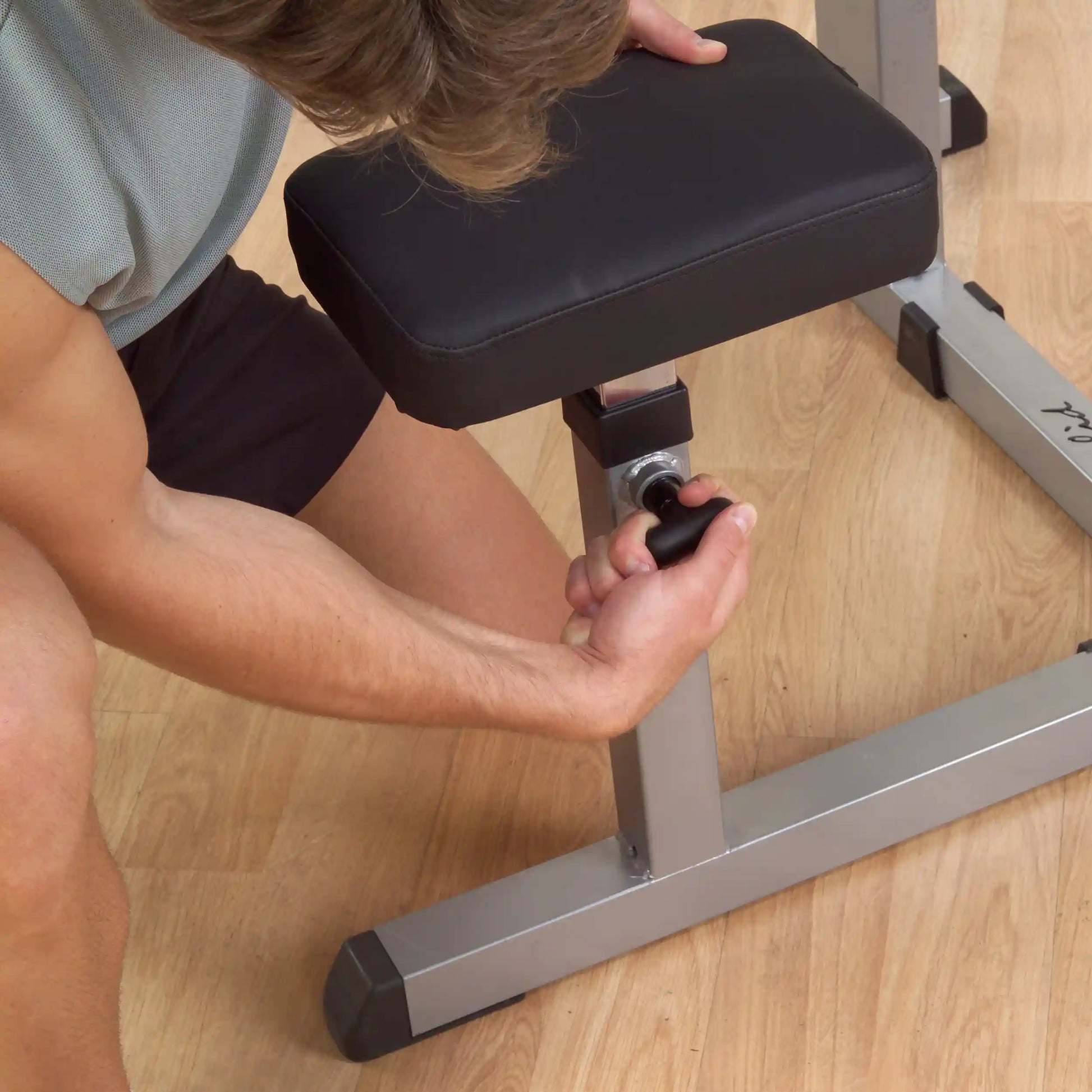 Adjusting the height of a black padded exercise bench with a silver frame.