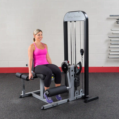 Woman using Body-Solid leg extension machine in gym, wearing pink tank top.