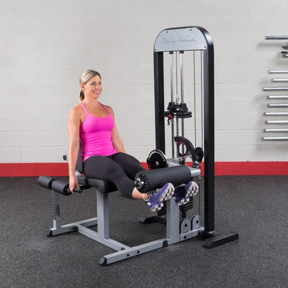 Woman using Body-Solid leg extension machine in pink tank top, black leggings.
