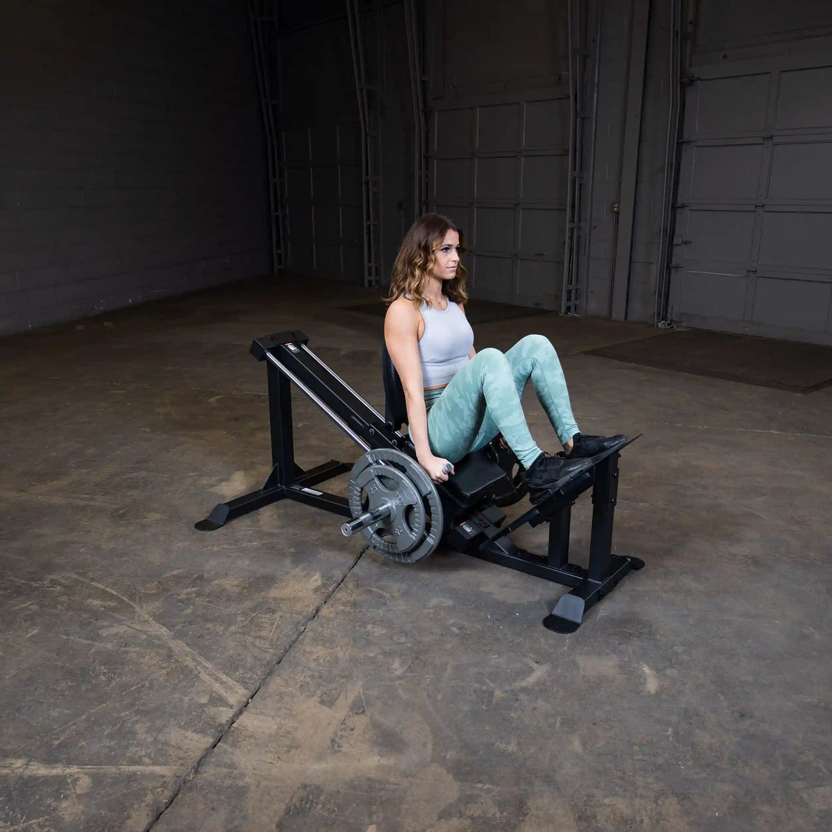Woman using a black leg press machine with weights in a gym.