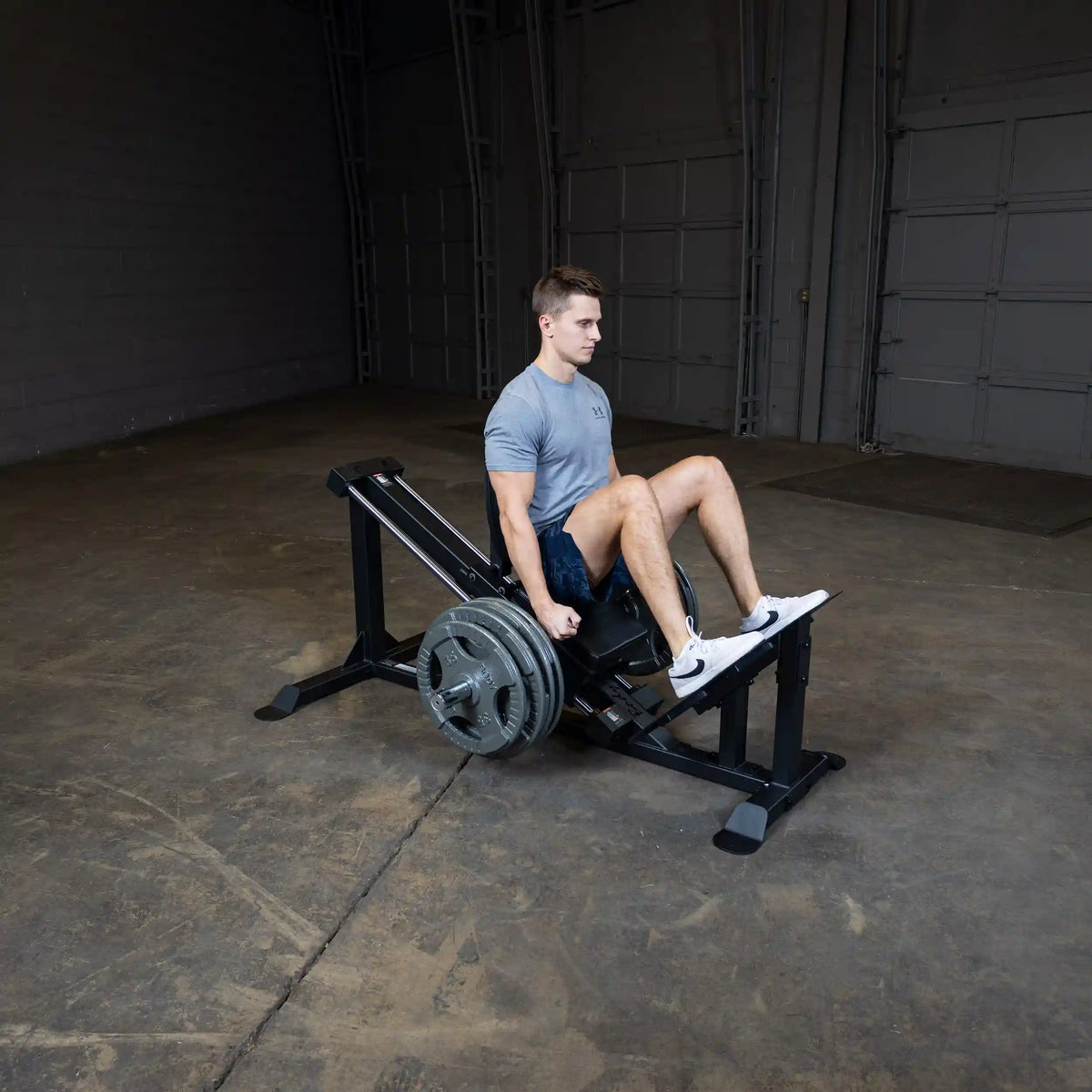 Man using leg press machine in a gym wearing a gray Under Armour shirt.