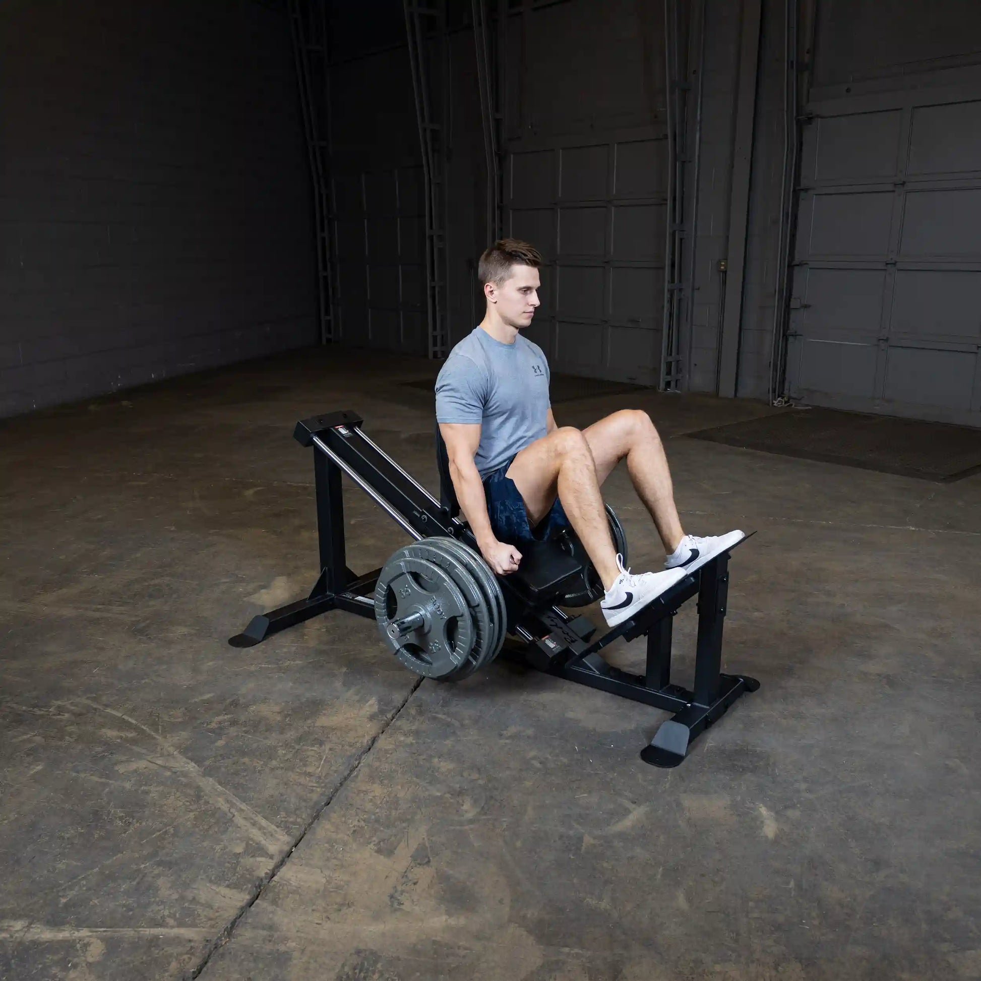 Man using leg press machine in a gym wearing a gray Under Armour shirt.