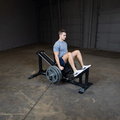 Man using leg press machine in a gym wearing a gray Under Armour shirt.