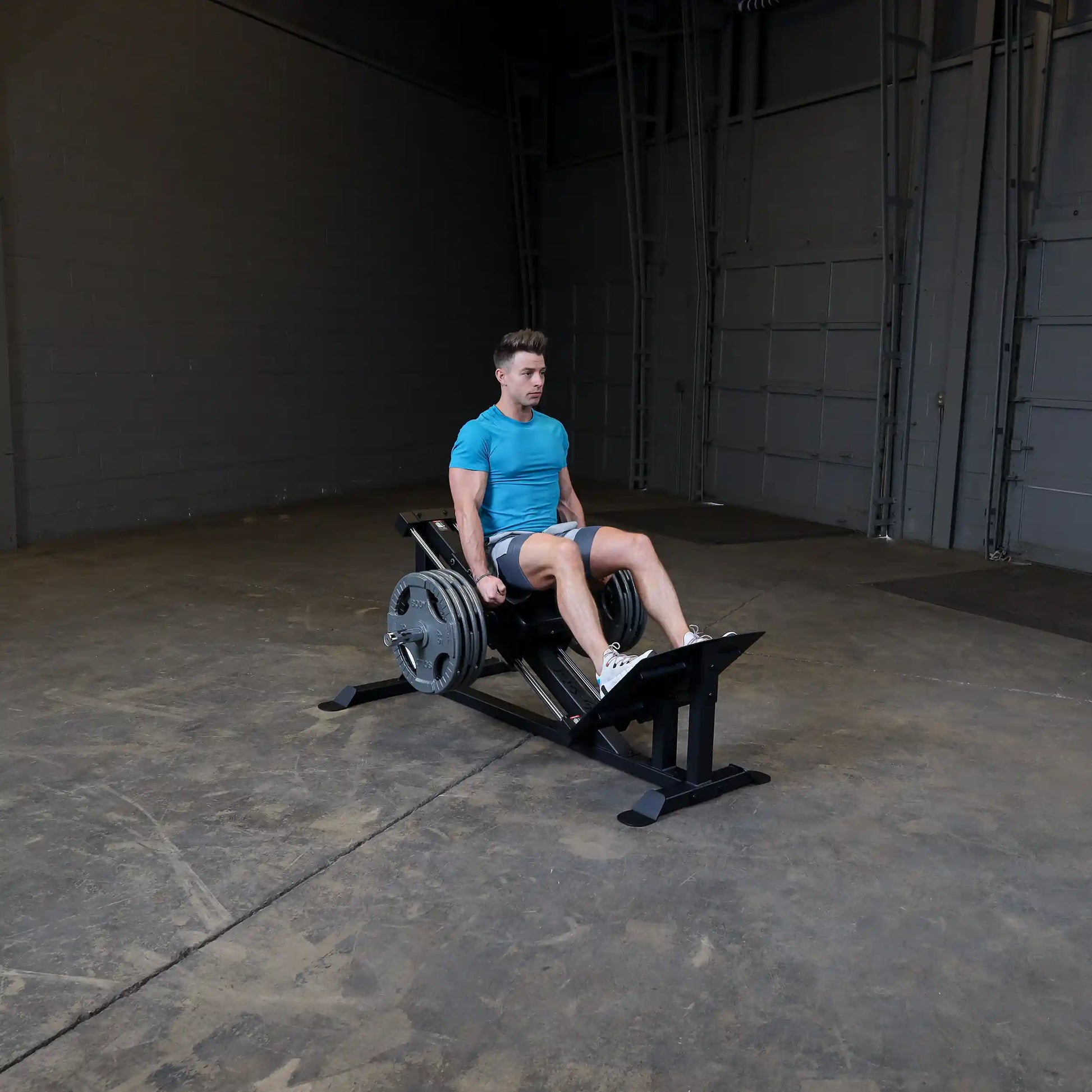 Man in blue shirt using a leg press machine in a gym.