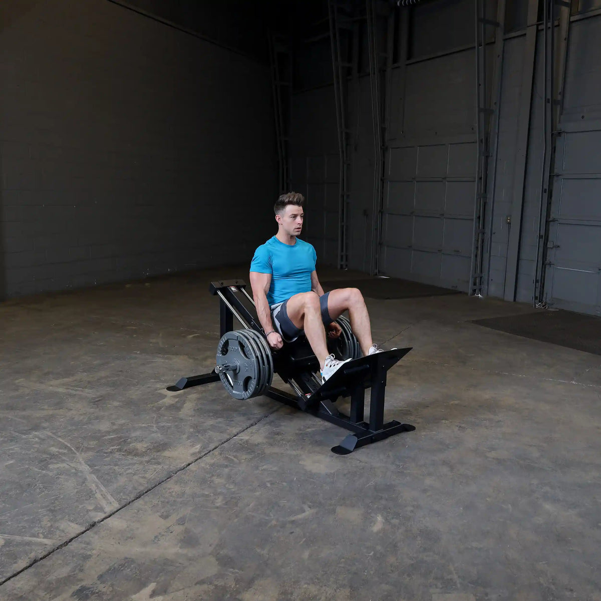 Man using leg press machine in gym wearing blue shirt and shorts for strength training.