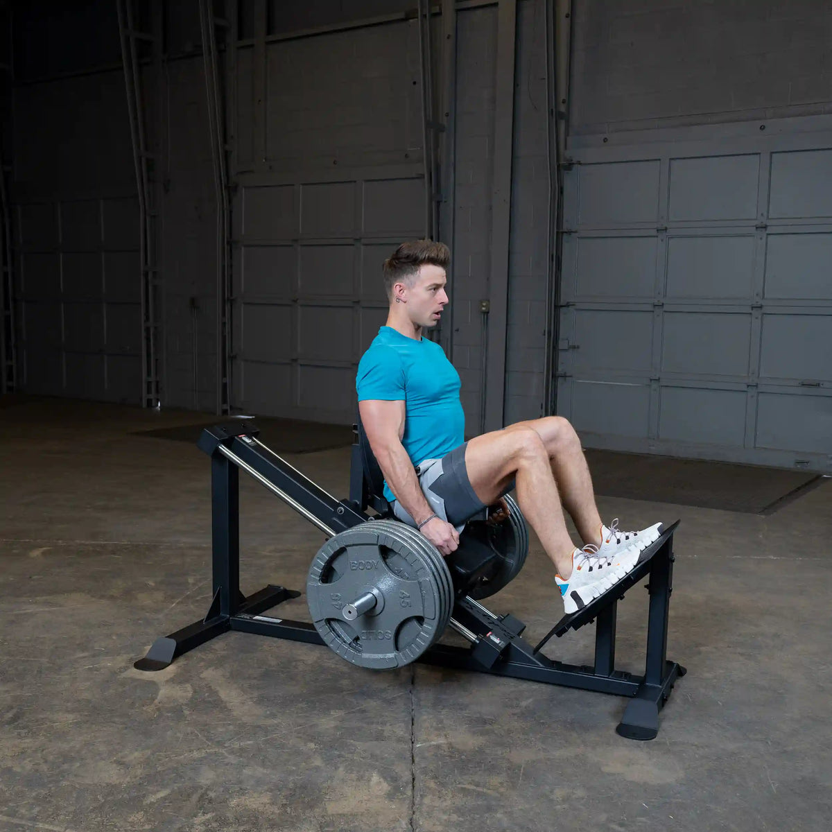 Man exercising on a leg press machine wearing a blue shirt in a gym.