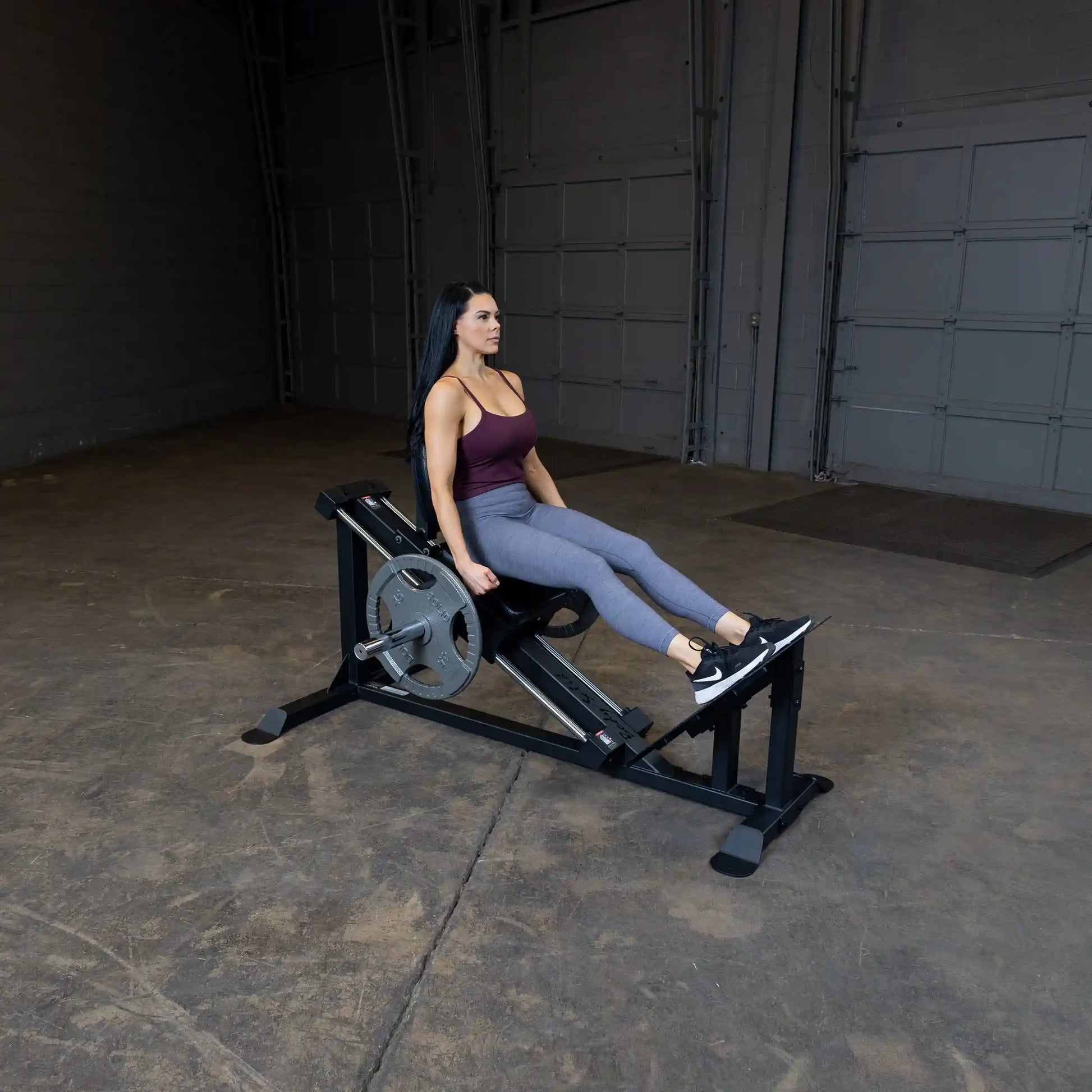 Woman using a seated calf raise machine in a gym, wearing a burgundy top and gray leggings.