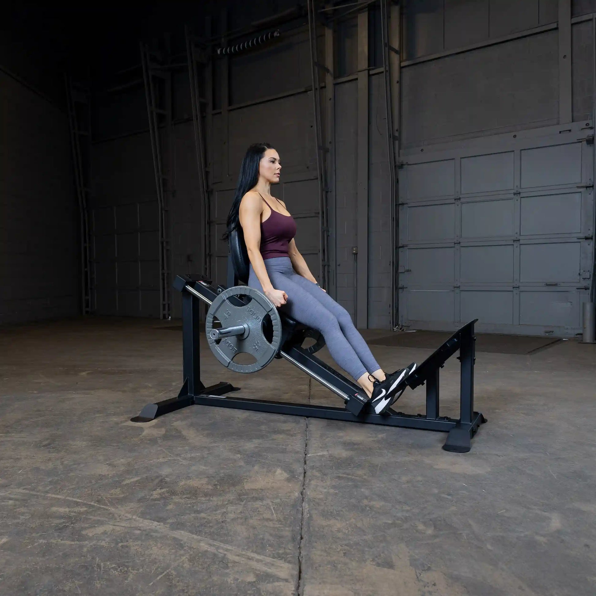 Woman using leg press machine in industrial gym setting.