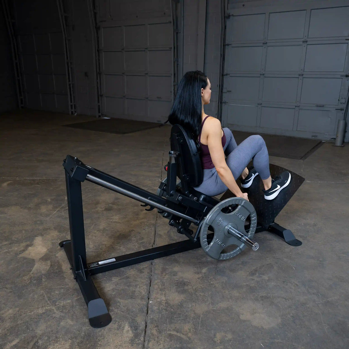 Woman using a black leg press machine in a gym setting.