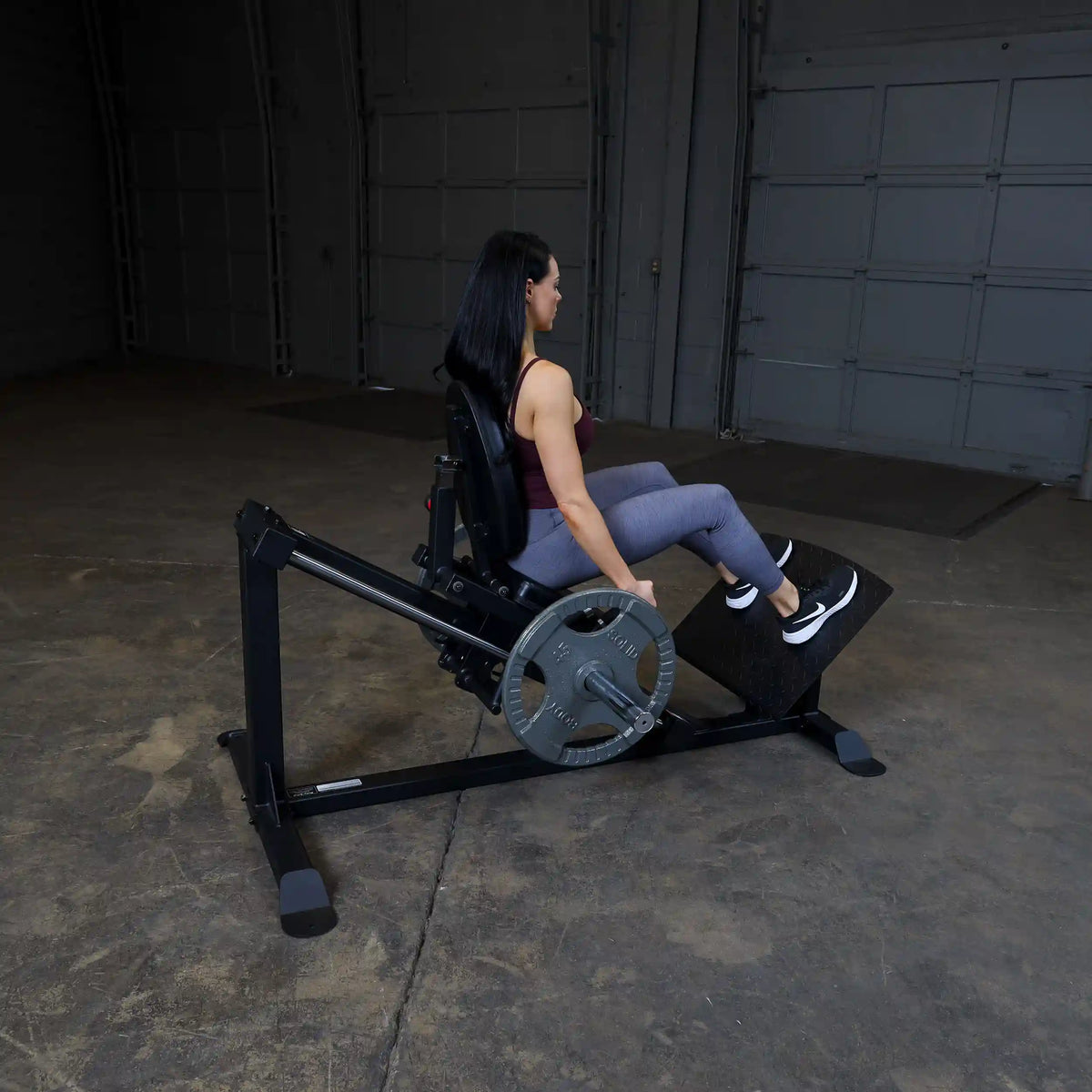 Woman using  leg press machine in a gym, wearing gray leggings and black sneakers.