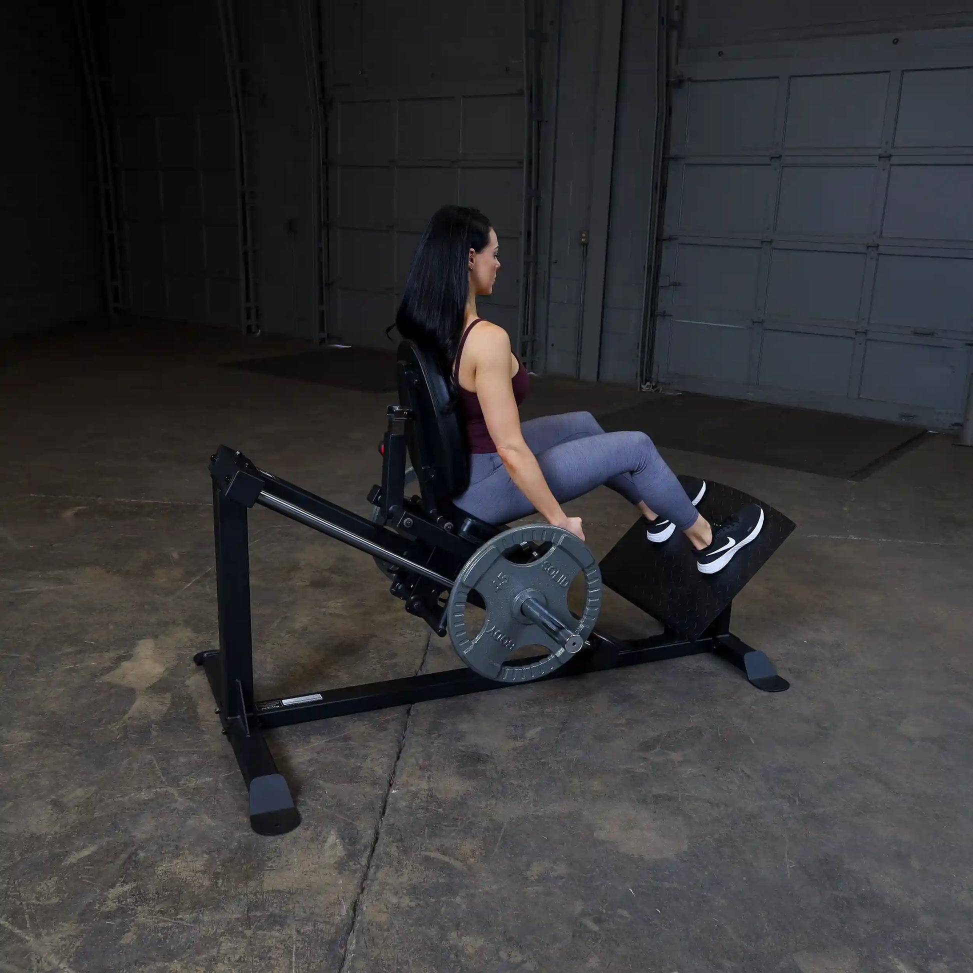 Woman using  leg press machine in a gym, wearing gray leggings and black sneakers.