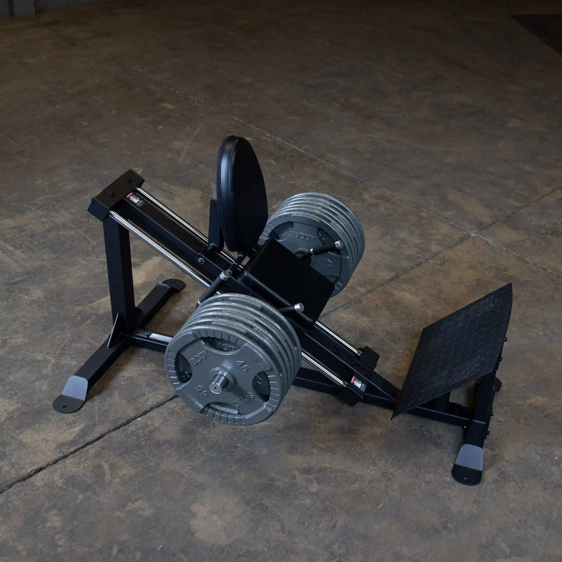 Rogue Fitness leg press machine with heavy weight plates on a gym floor.