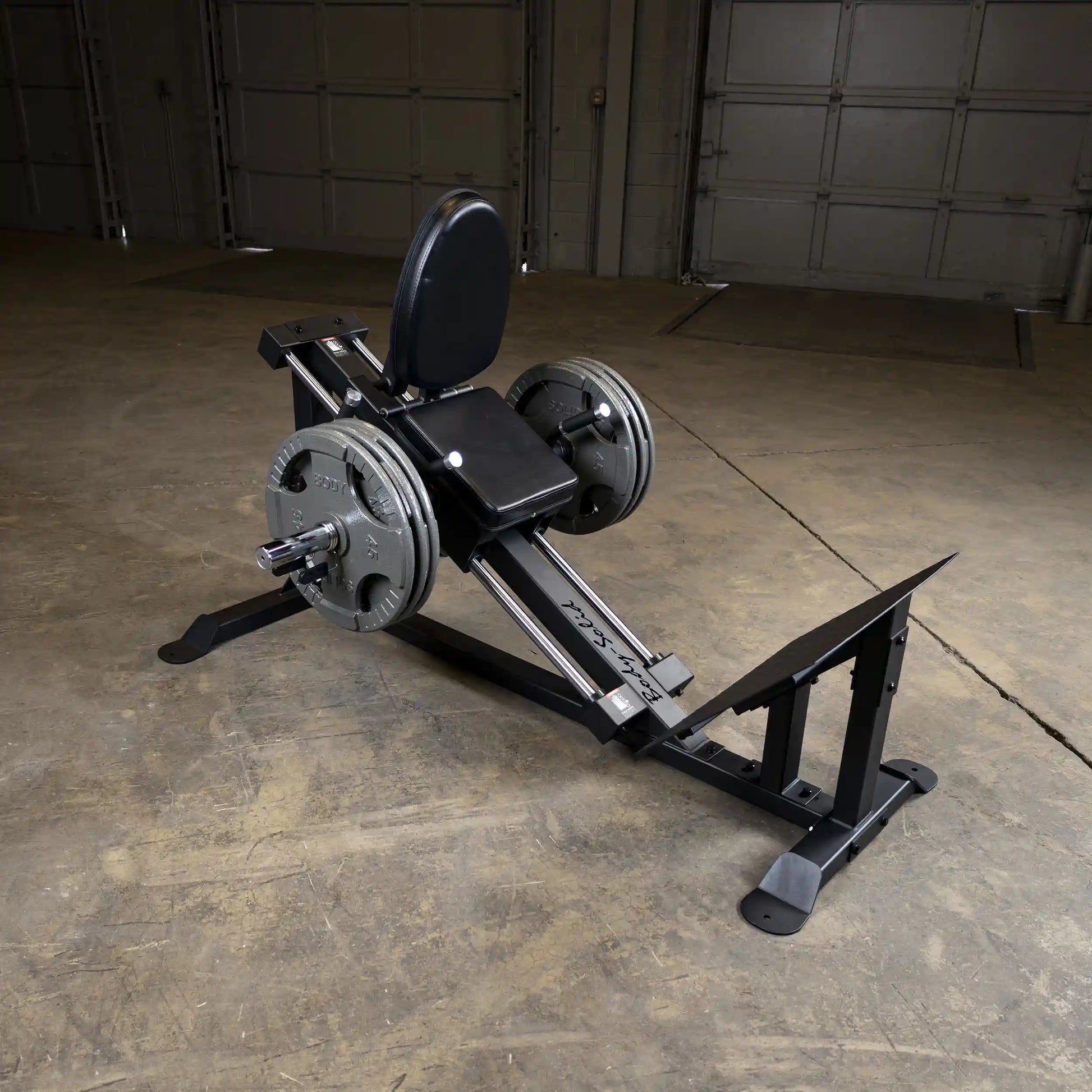 Body-Solid compact leg sled with weight plates in a garage gym setup.