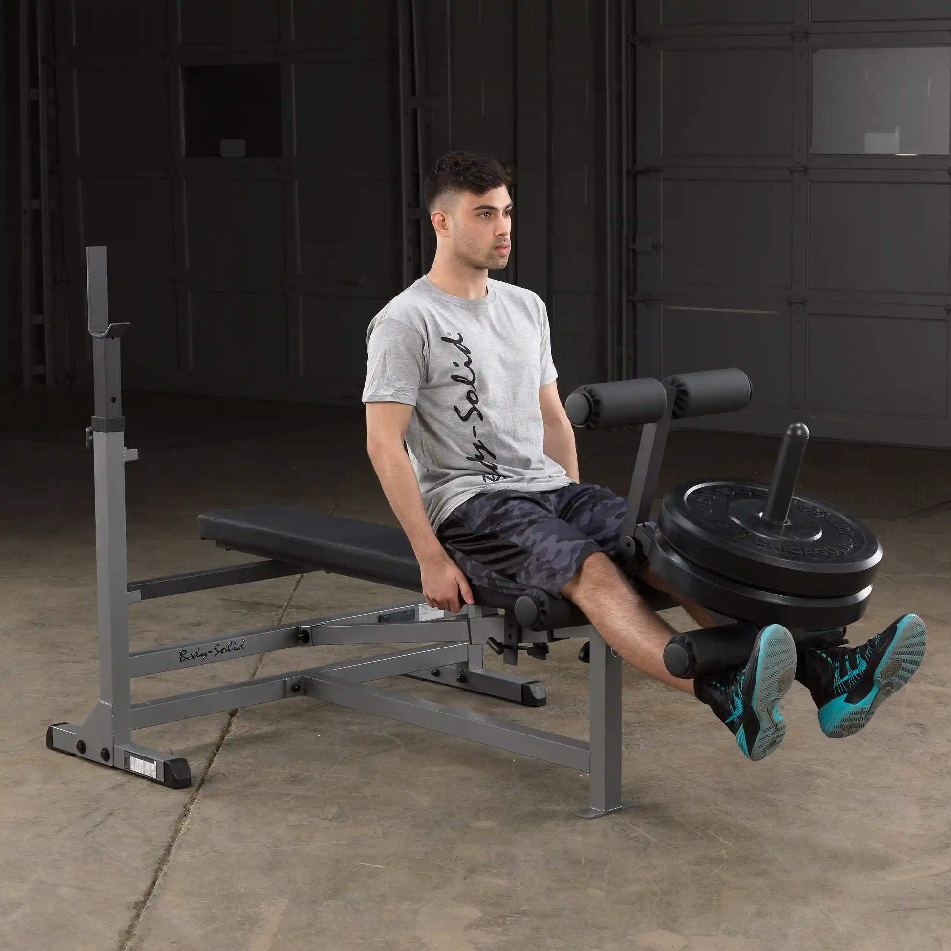 Man using Body-Solid weight bench for leg exercises in a garage gym.