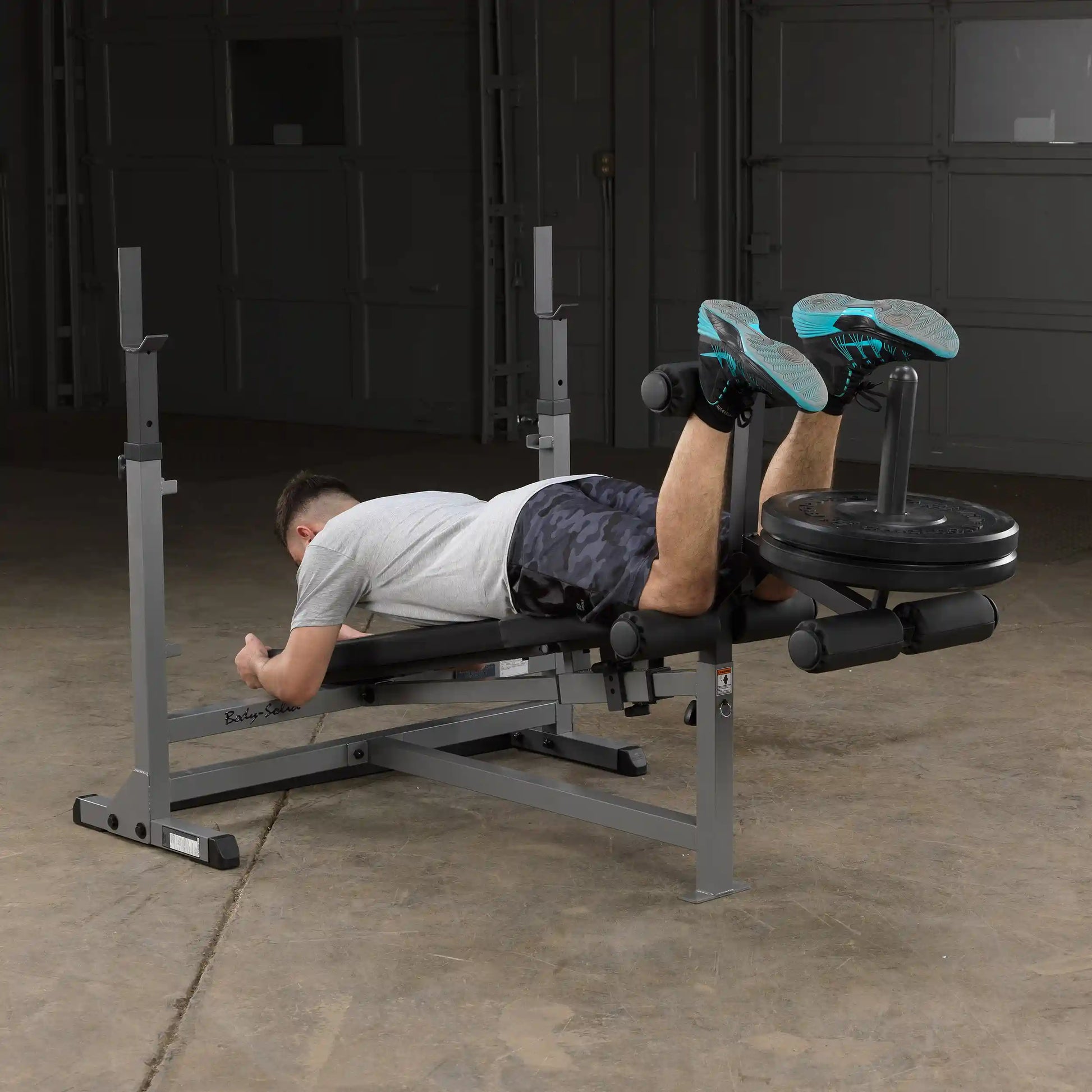 Man using leg curl machine with weight plates in a gym.