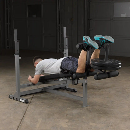 Man using leg curl machine with weight plates in a gym.