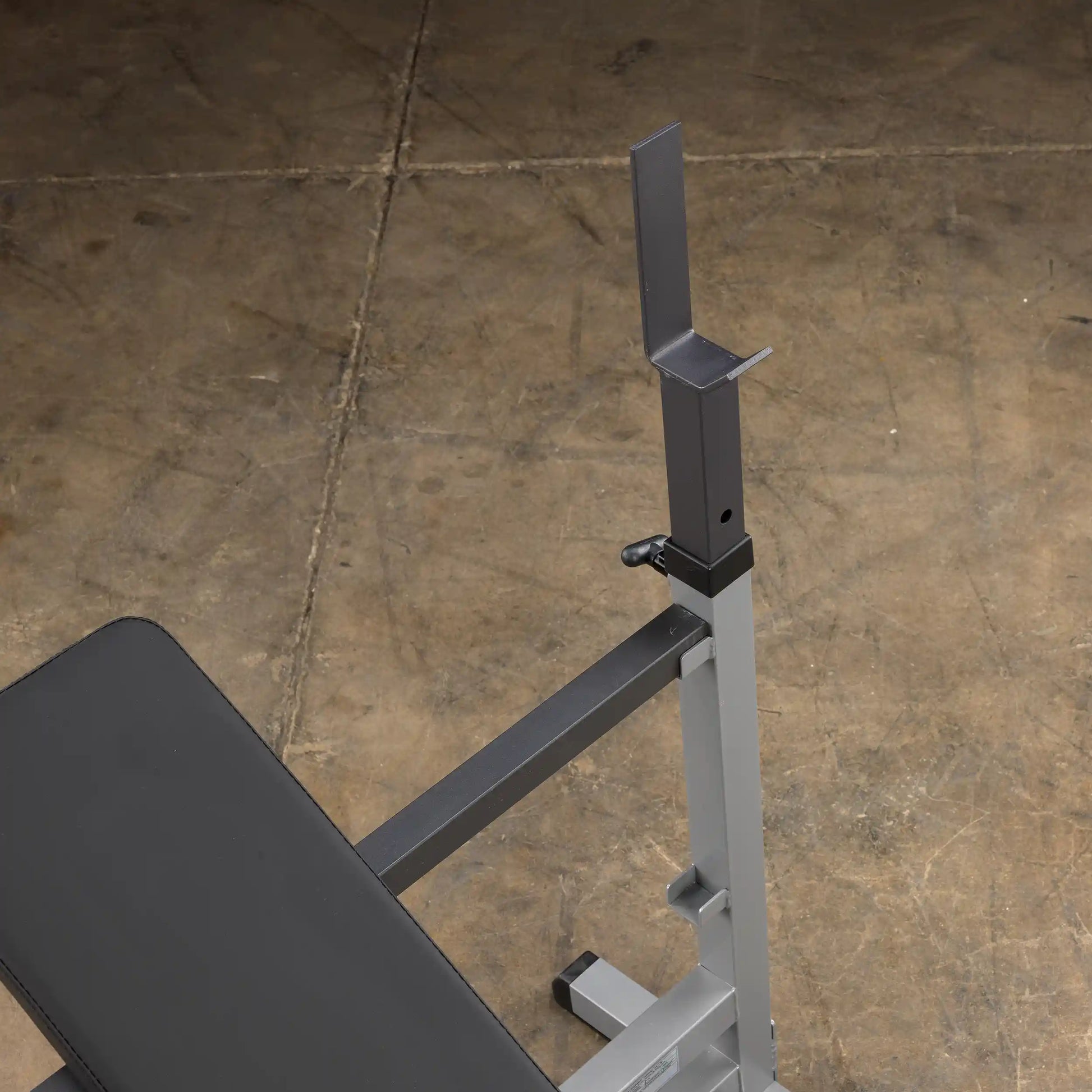Adjustable weight bench rack with black padding on concrete floor.