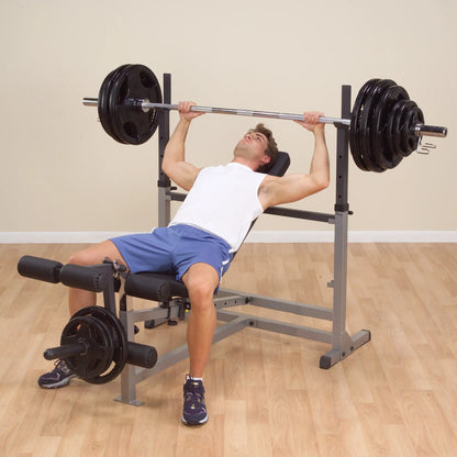 Man lifting weights on adjustable bench press with blue shorts and white tank top.