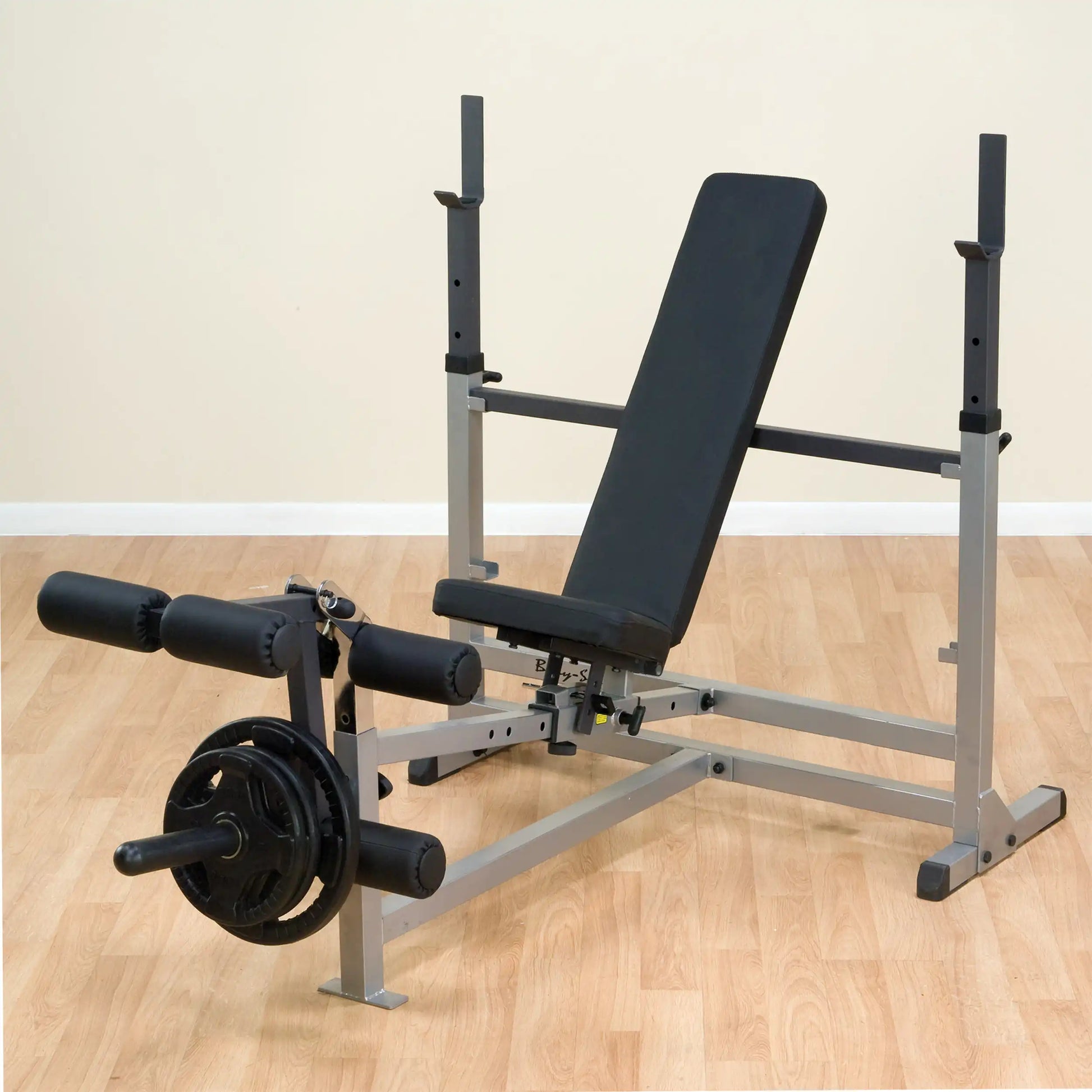 Adjustable weight bench with leg developer on wooden floor.