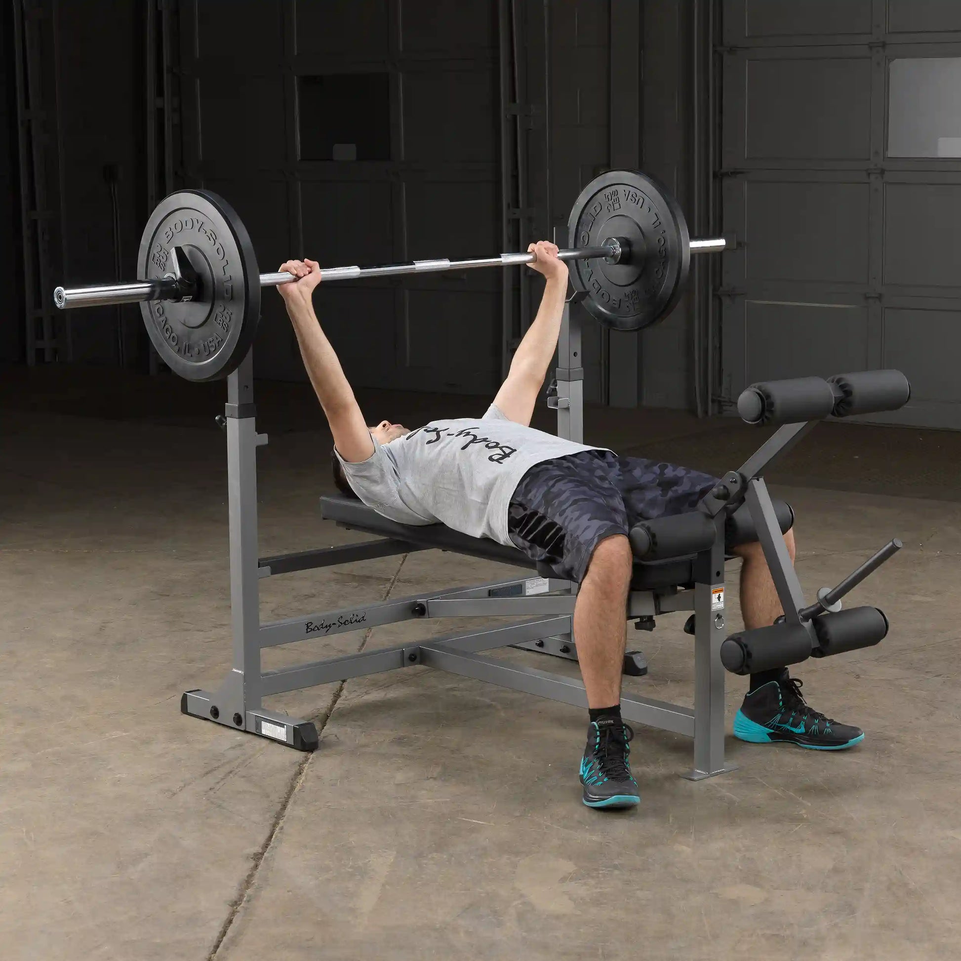 Man lifting weights on Body-Solid bench press with leg extension in a gym.