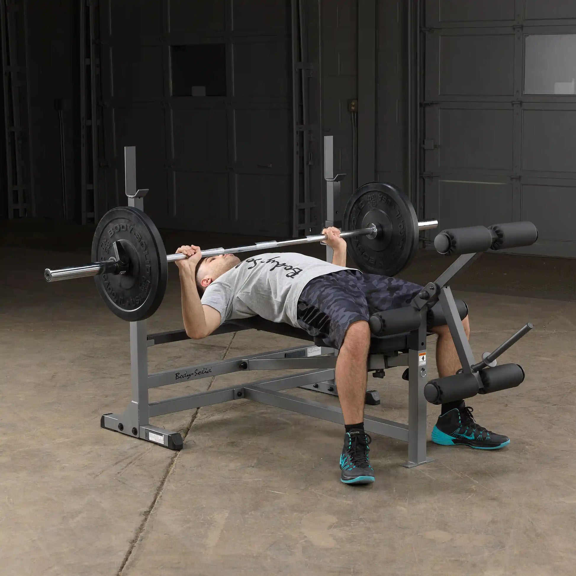 Man bench pressing on Body-Solid weight bench with black weights in a gym.