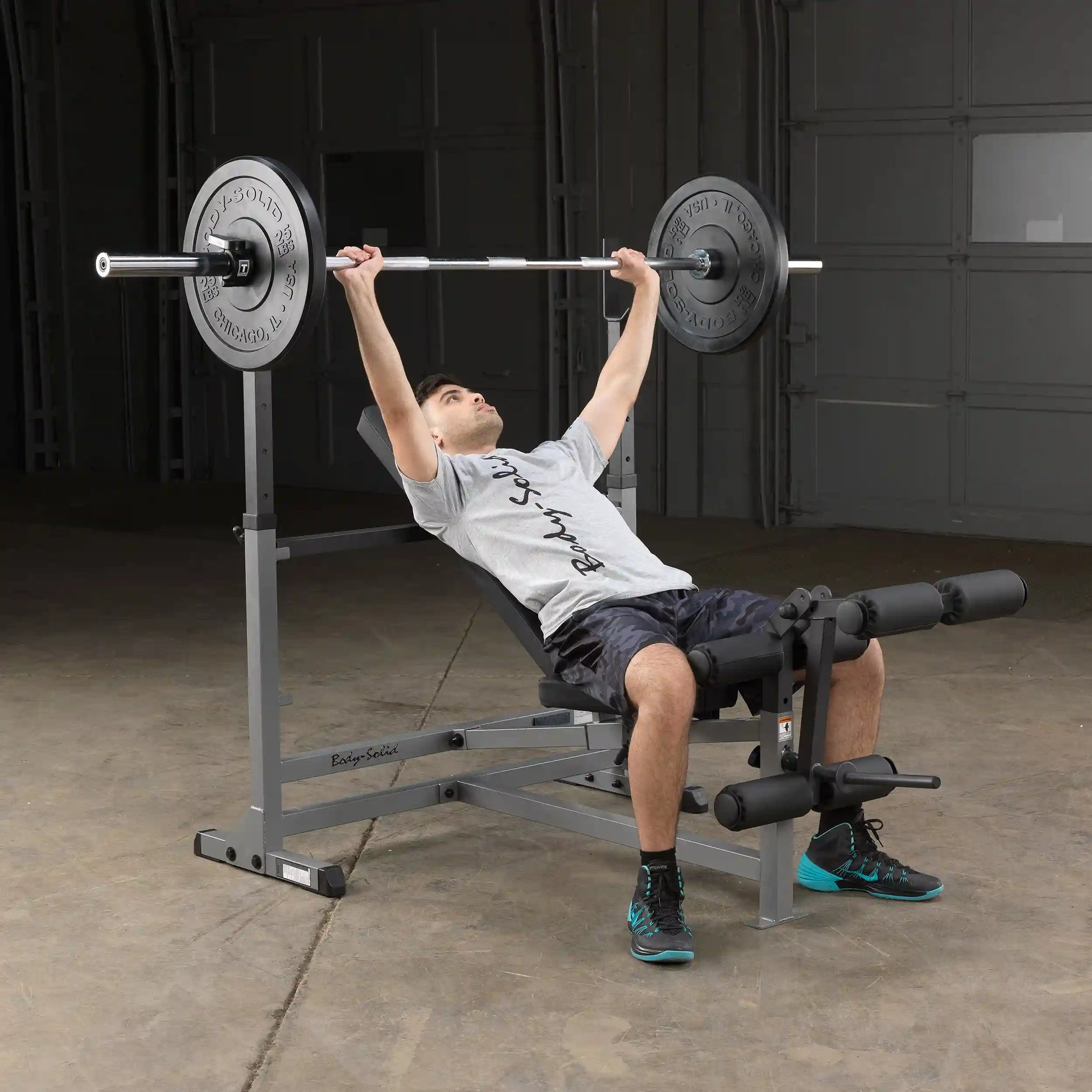 Man using Body-Solid weight bench with barbell in a garage gym.