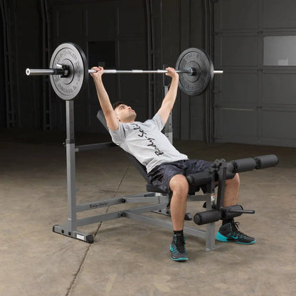 Man using Body-Solid weight bench with barbell in a garage gym.
