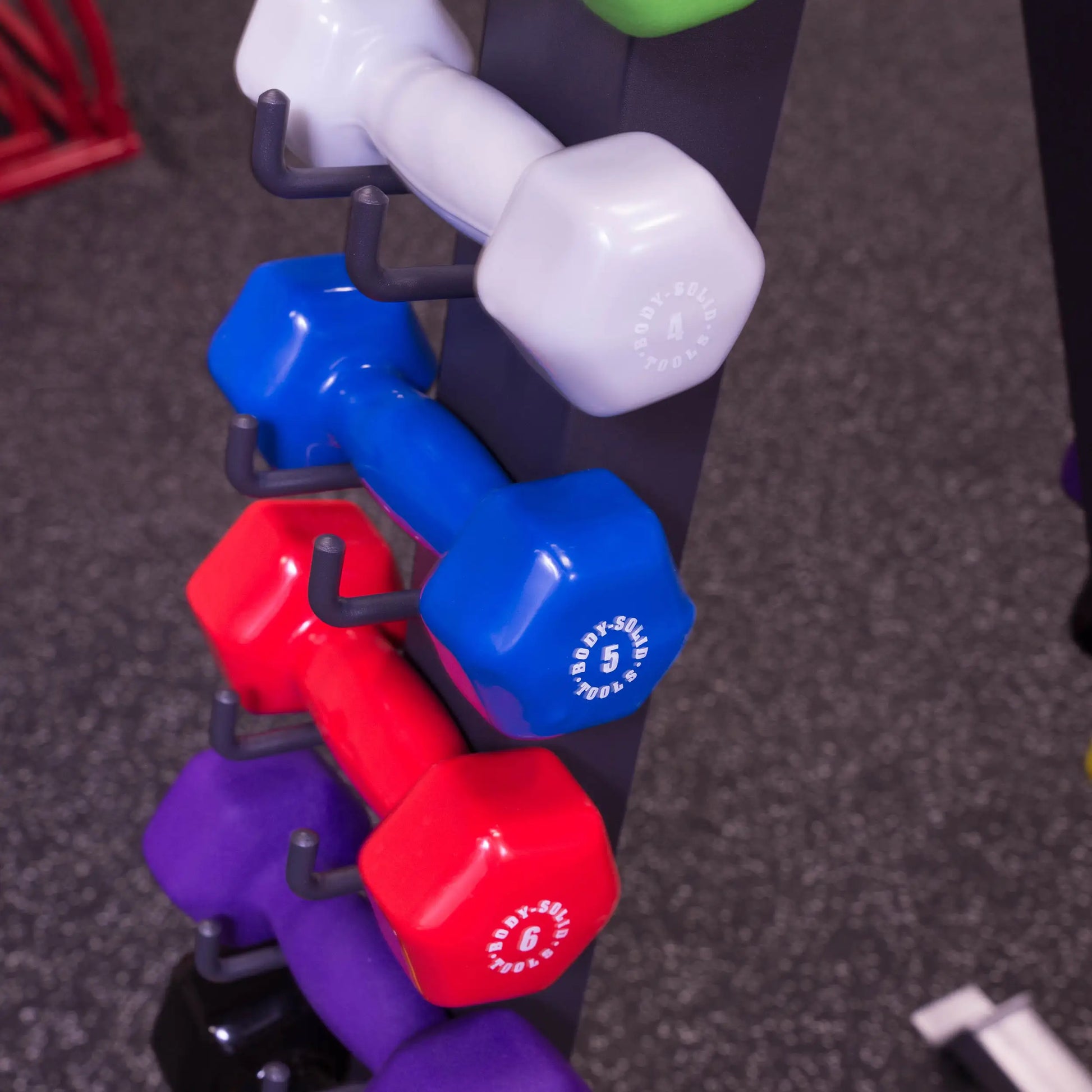 Colorful hex dumbbells on rack in gym, featuring Body-Solid brand weights.