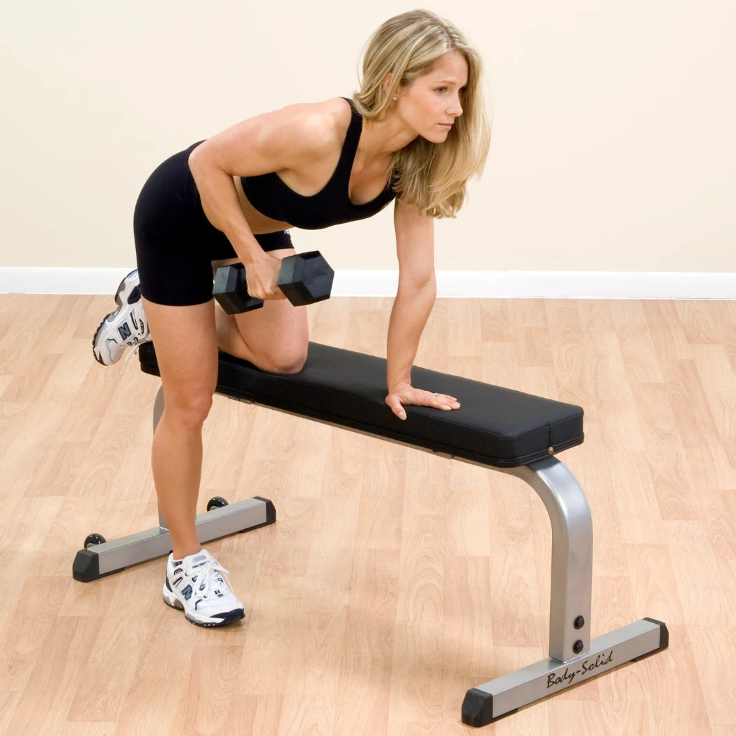 Woman using dumbbell on Body-Solid bench for strength training.