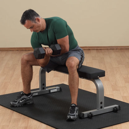 Man in green shirt performing dumbbell curls on a flat weight bench, emphasizing arm workout.