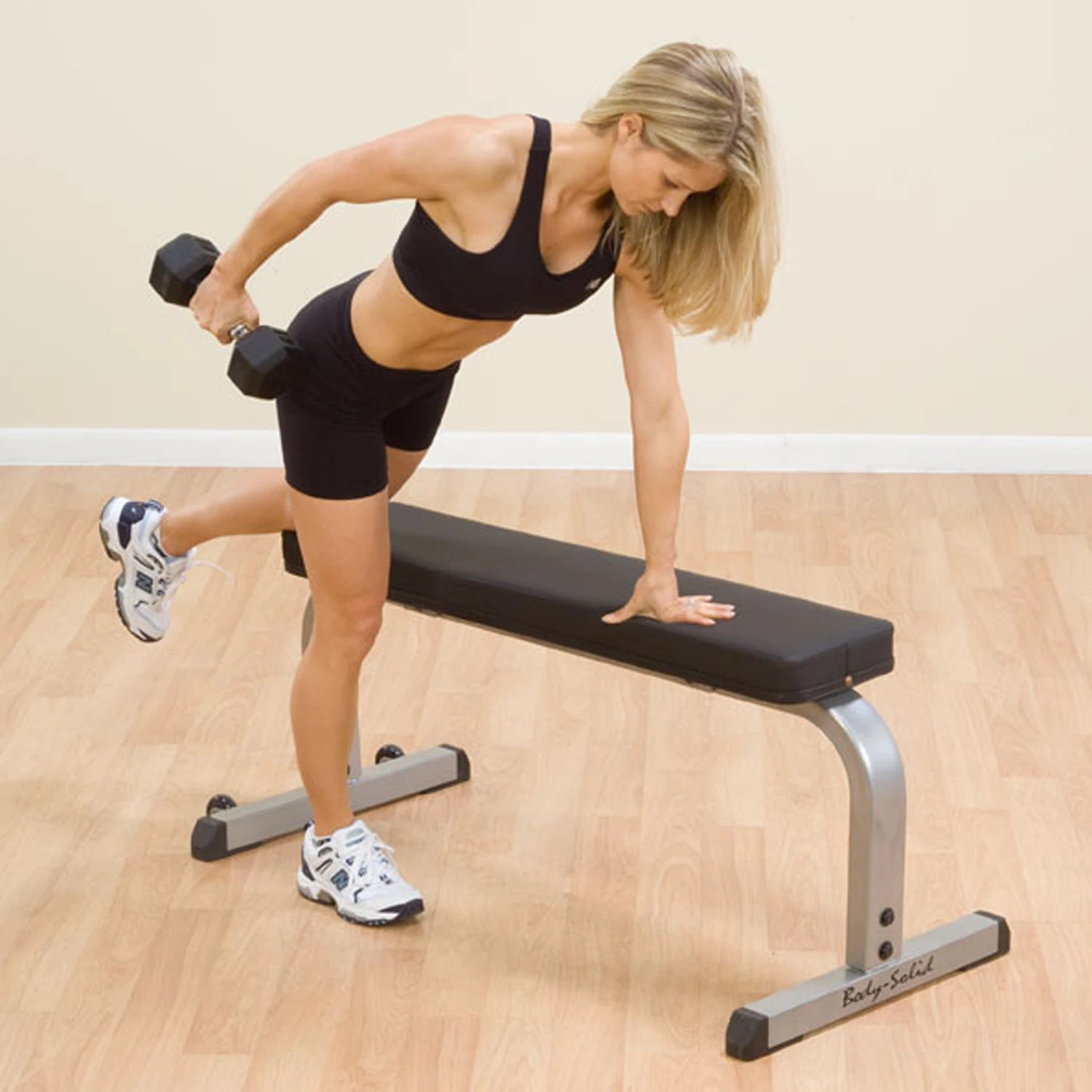 Woman performing tricep kickback with dumbbell on Body-Solid bench.