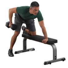 Man performing dumbbell row on a black workout bench, wearing green shirt and gray shorts.
