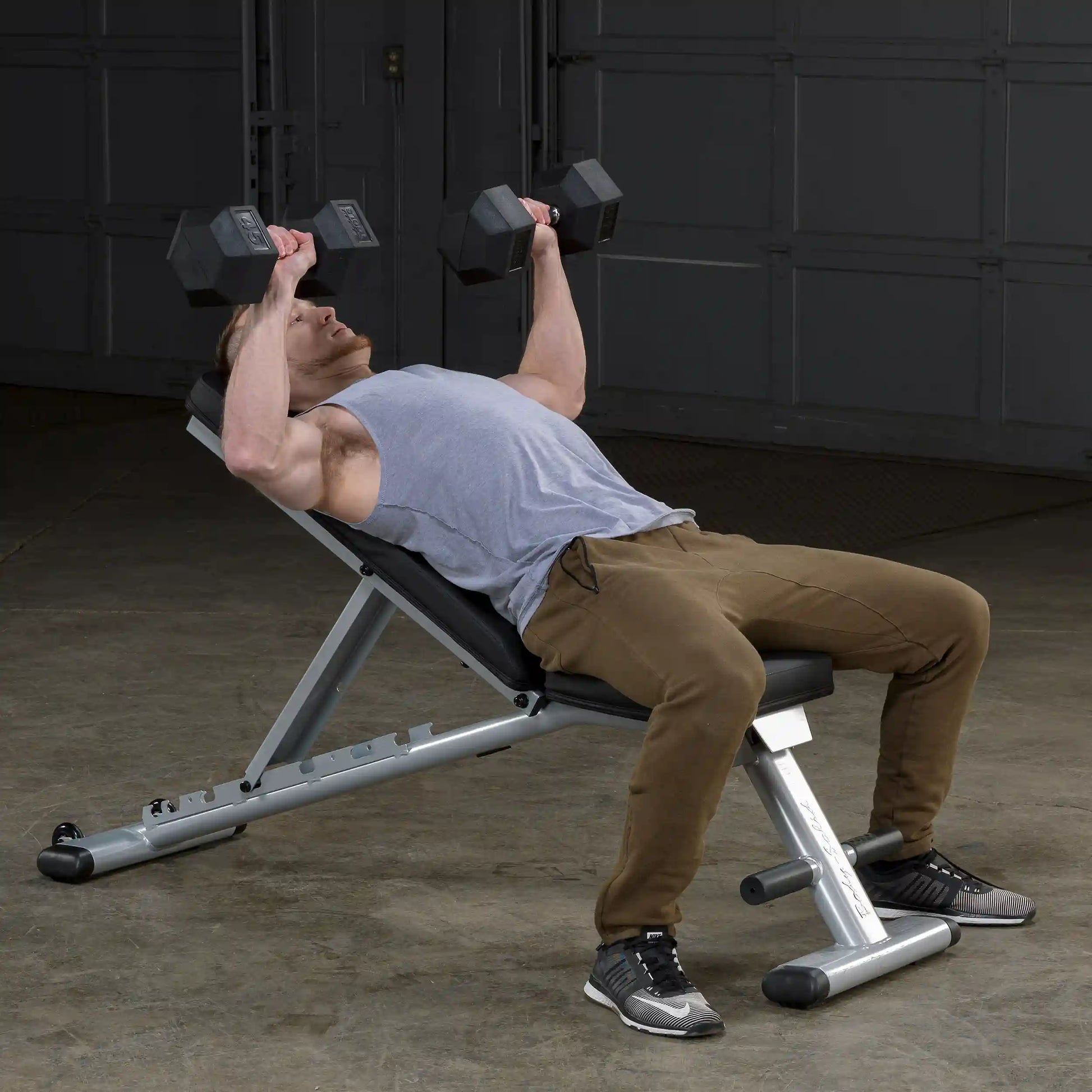 Man lifting dumbbells on adjustable weight bench in gym.