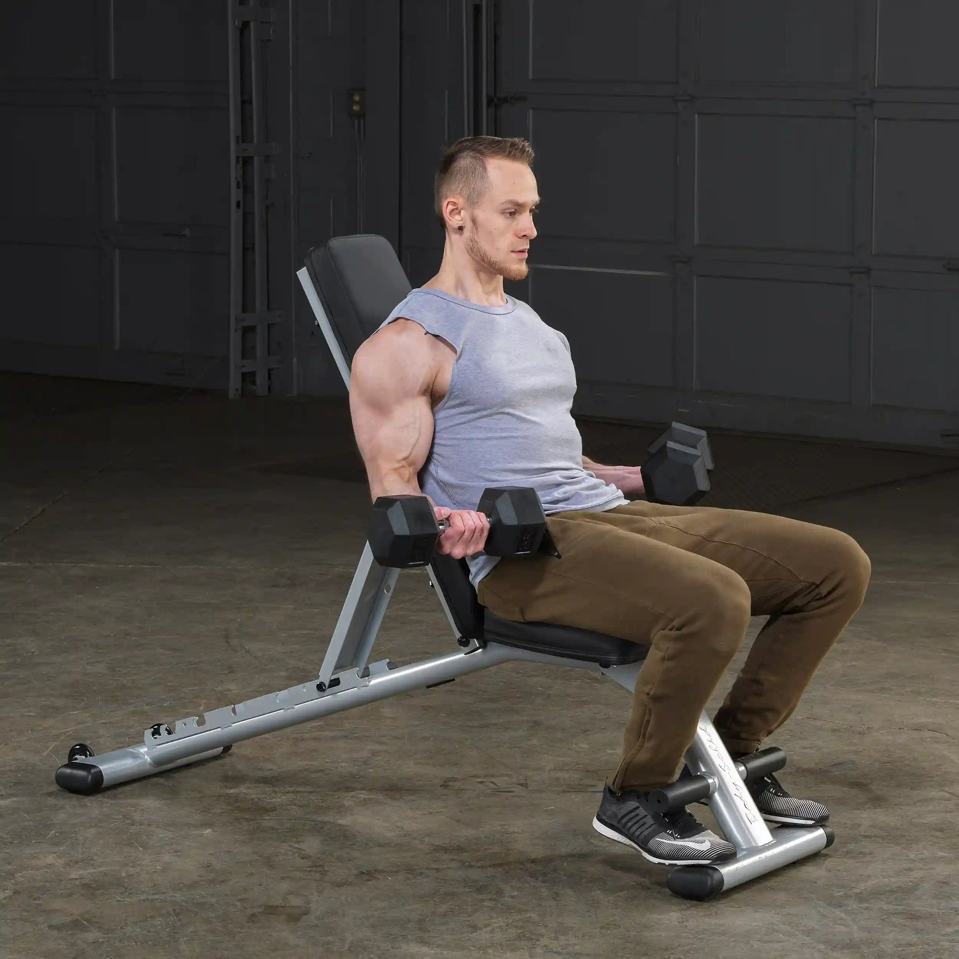 Man doing dumbbell curls on an adjustable weight bench in a garage gym.