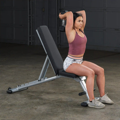 Woman performing tricep exercise on adjustable weight bench in gym.