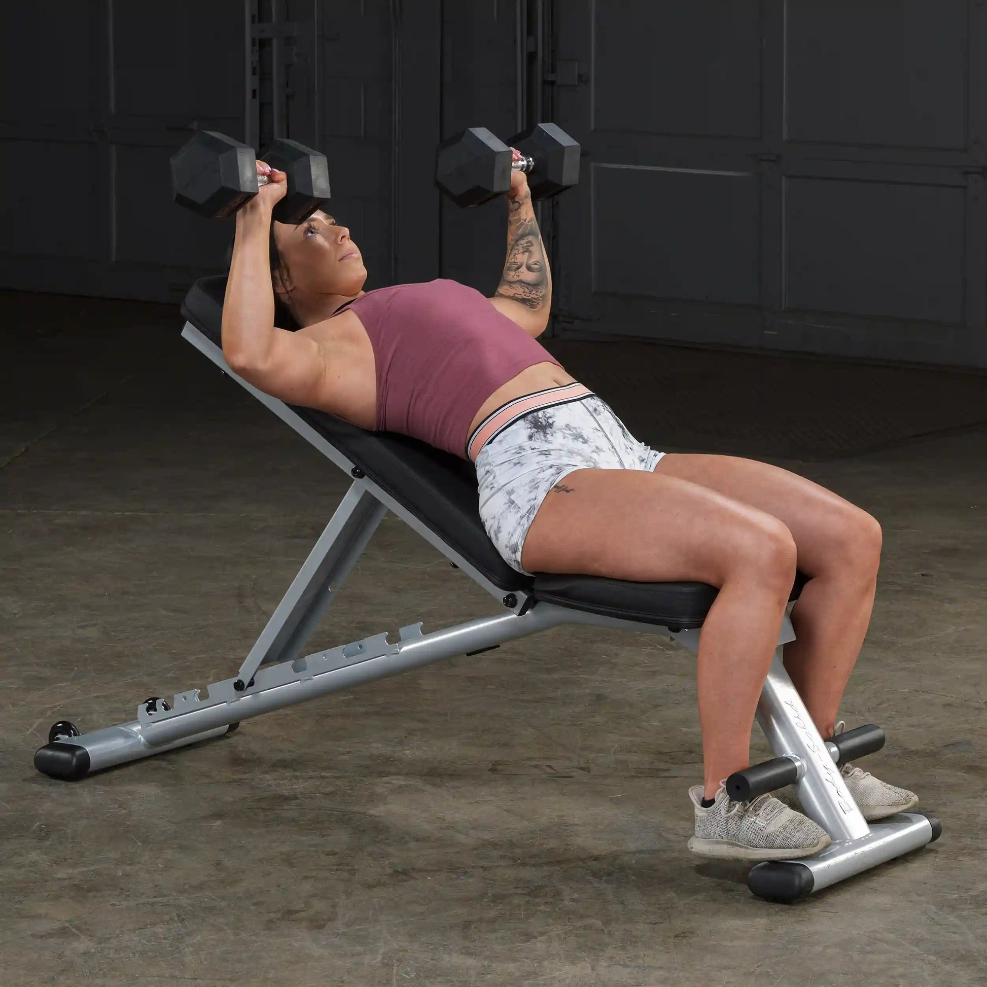 Woman performing dumbbell press on adjustable weight bench in gym.