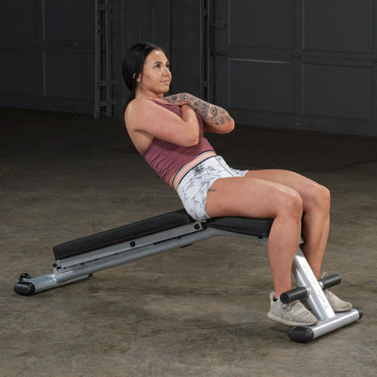 Woman performing sit-up on adjustable weight bench with tattooed arm and gray sneakers.