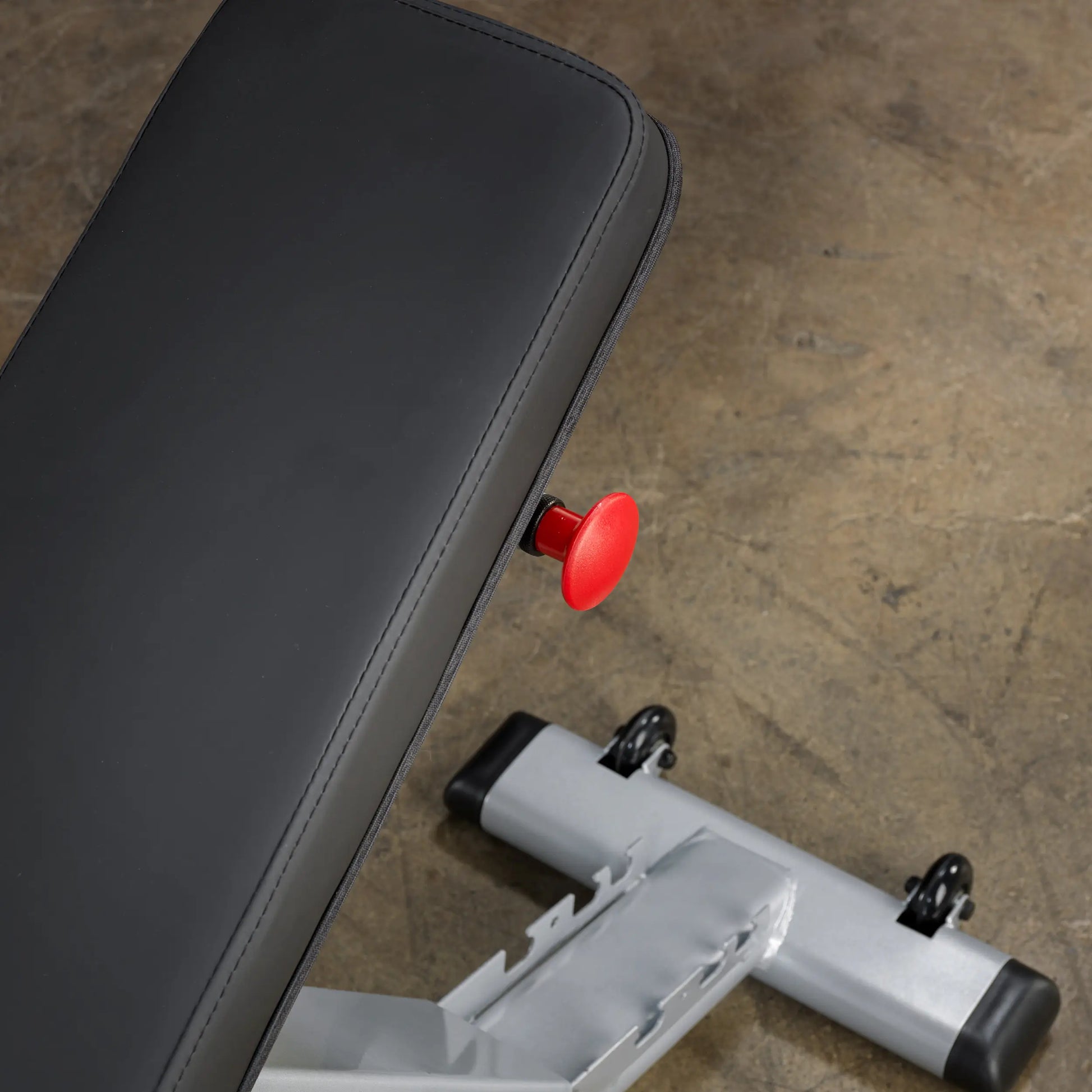 Adjustable weight bench with black padding and red adjustment knob on a concrete floor.