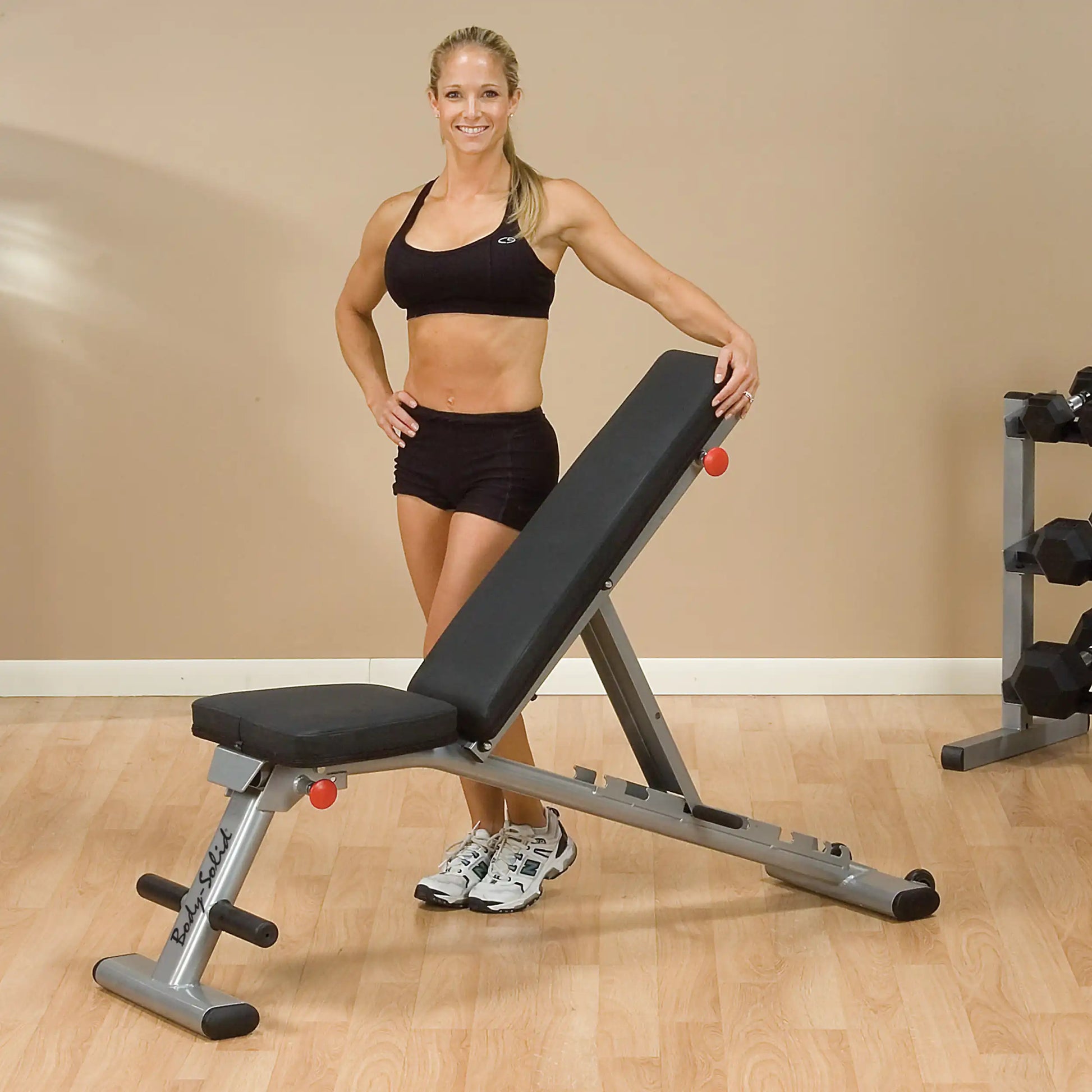 Woman posing with Body-Solid adjustable weight bench in home gym.