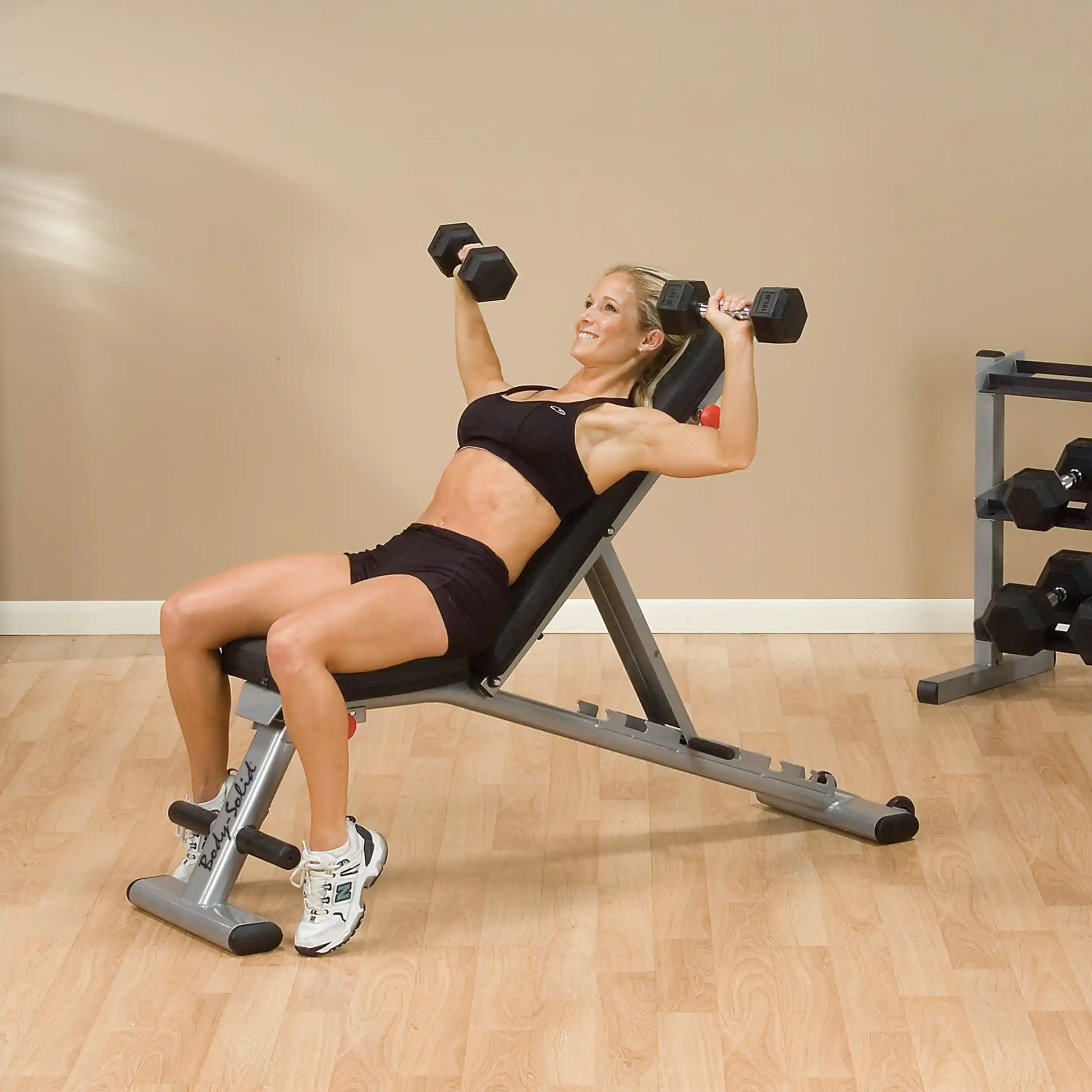 Woman performing dumbbell bench press on adjustable weight bench in gym.