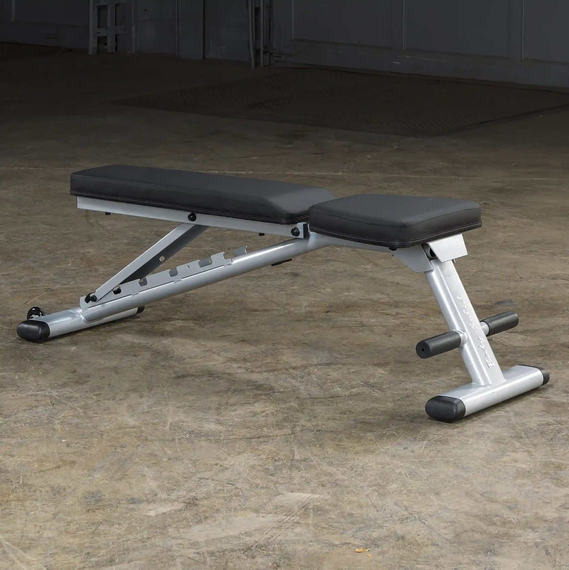 Adjustable weight bench with silver frame and black padding on a concrete floor.